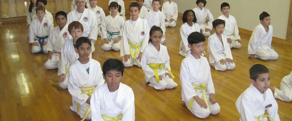 A group of young boys in white uniforms sitting on the floor.