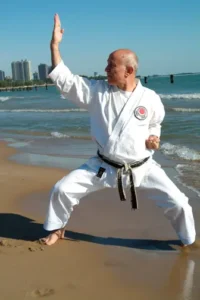 A man in white and black uniform practicing karate on the beach.